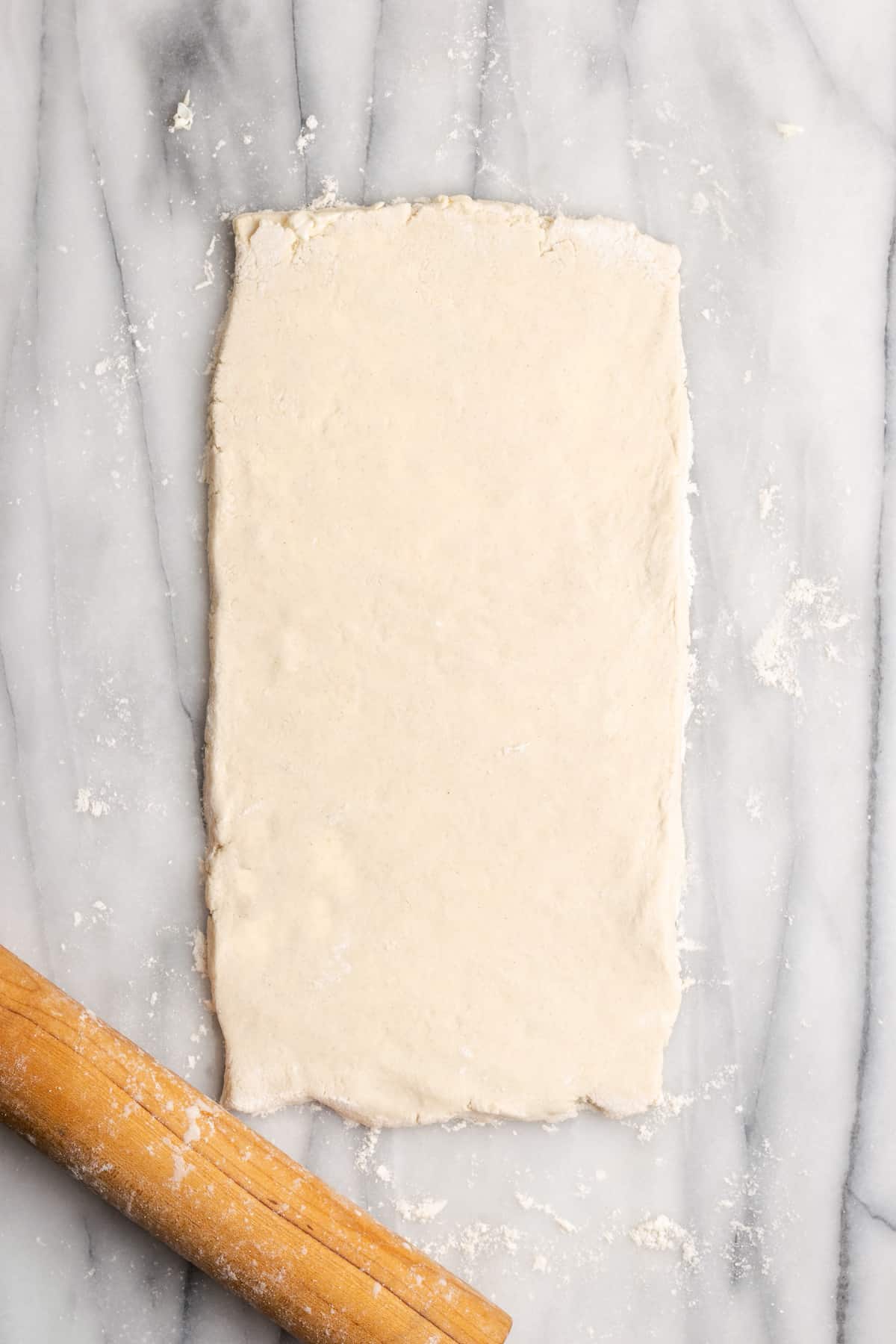 A slightly thick rectangle of dough rolled out next to a rolling pin