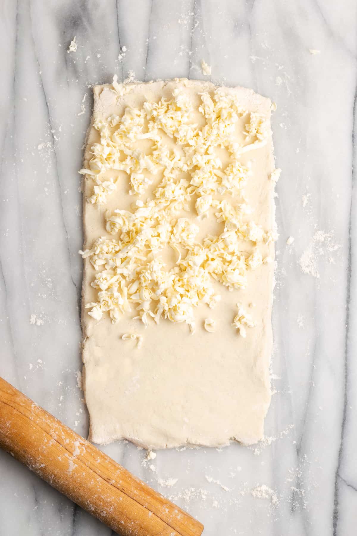 A slightly thick rectangle of dough with shredded butter covering two-thirds of it