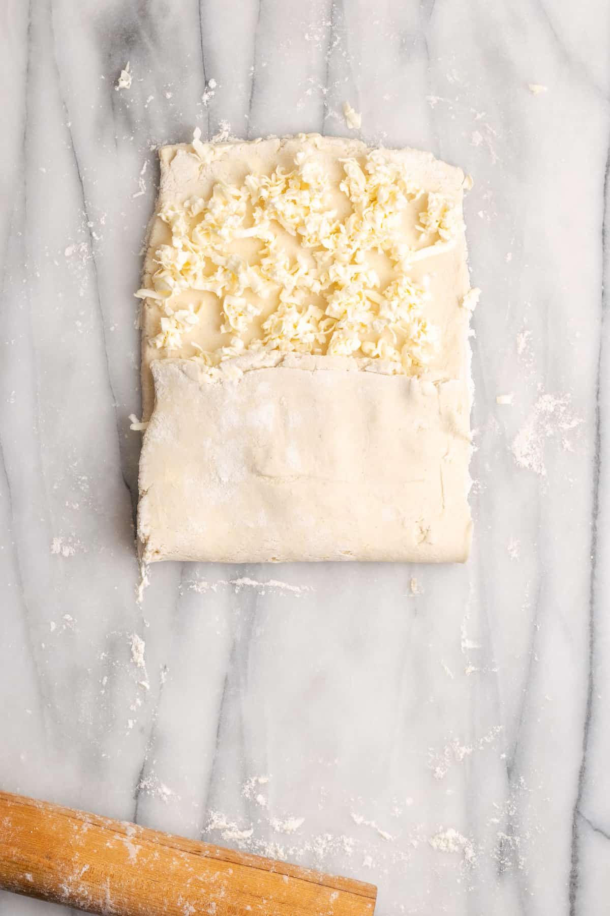 A rectangle of dough with shredded butter on top, with a third of the dough folded up