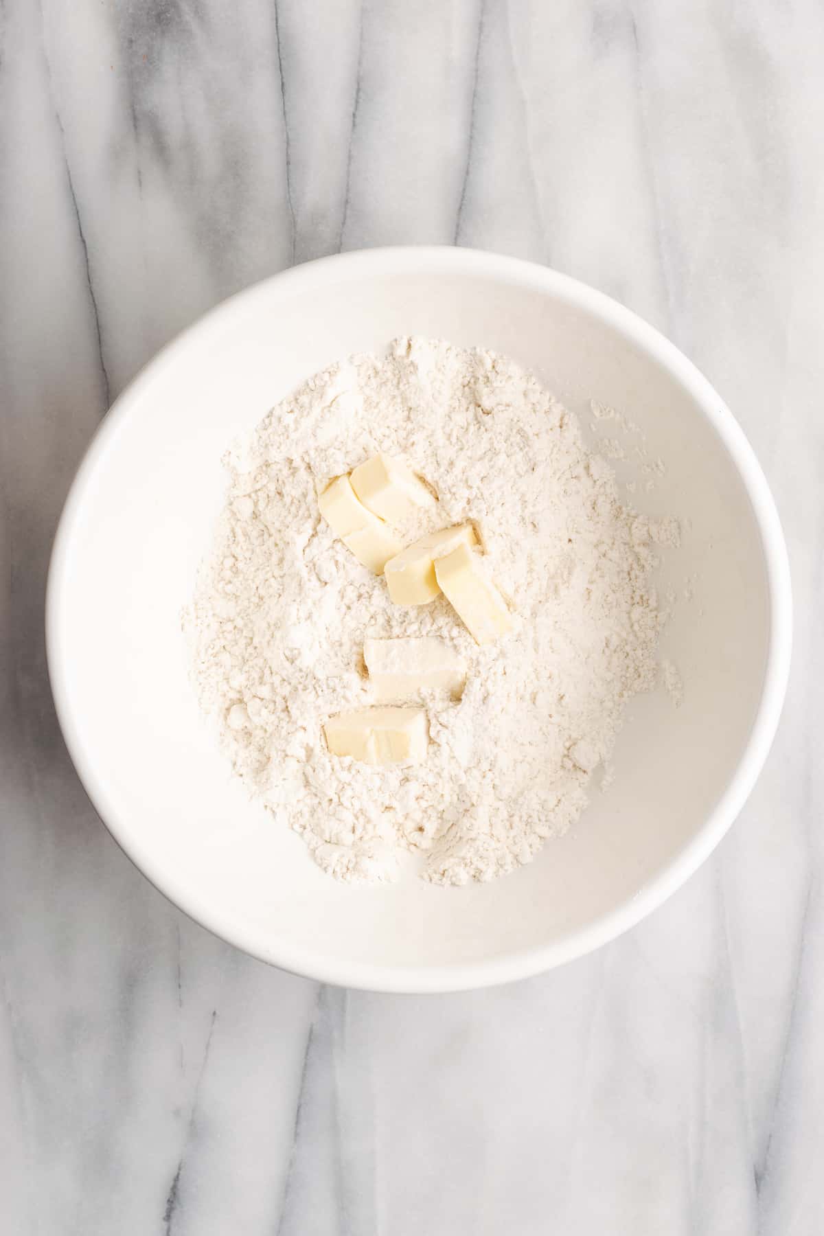 A mixing bowl with flour, salt, sugar, and chunks of vegan butter