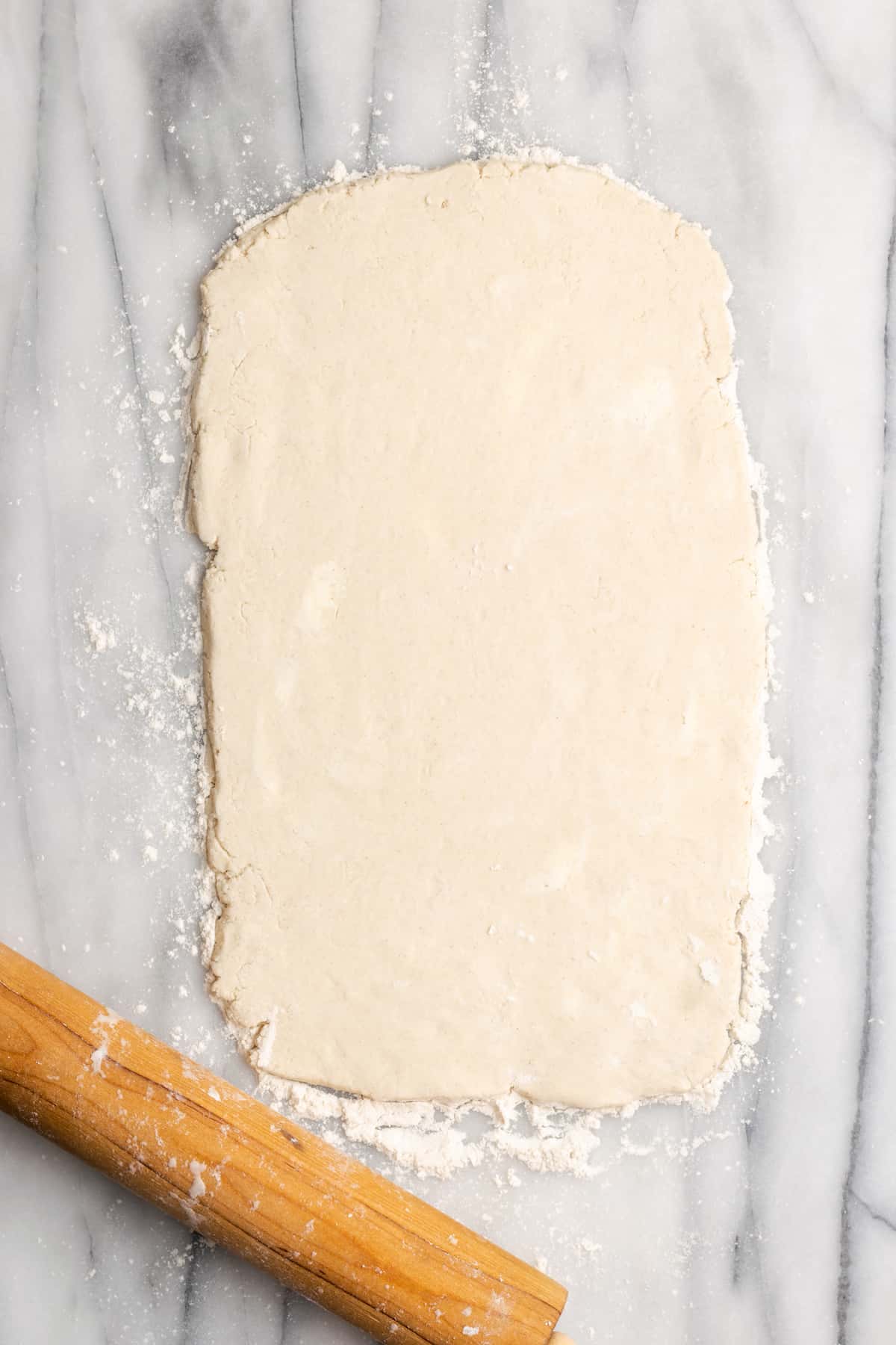 A thin rectangle of dough rolled out next to a rolling pin