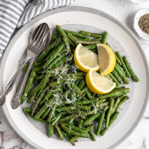 Overhead view of air fryer green beans on plate with spoon, fork, and lemon wedges
