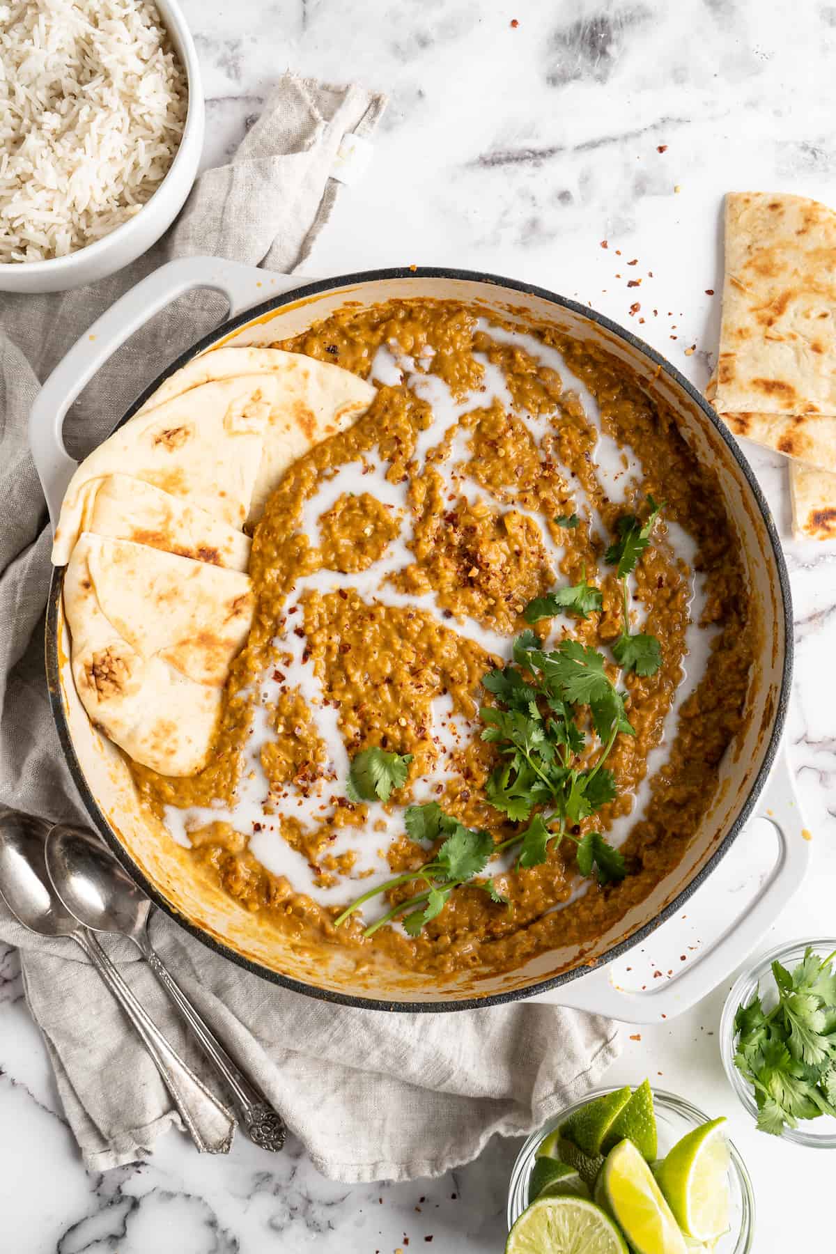 Pot of red lentil curry garnished with naan and cilantro