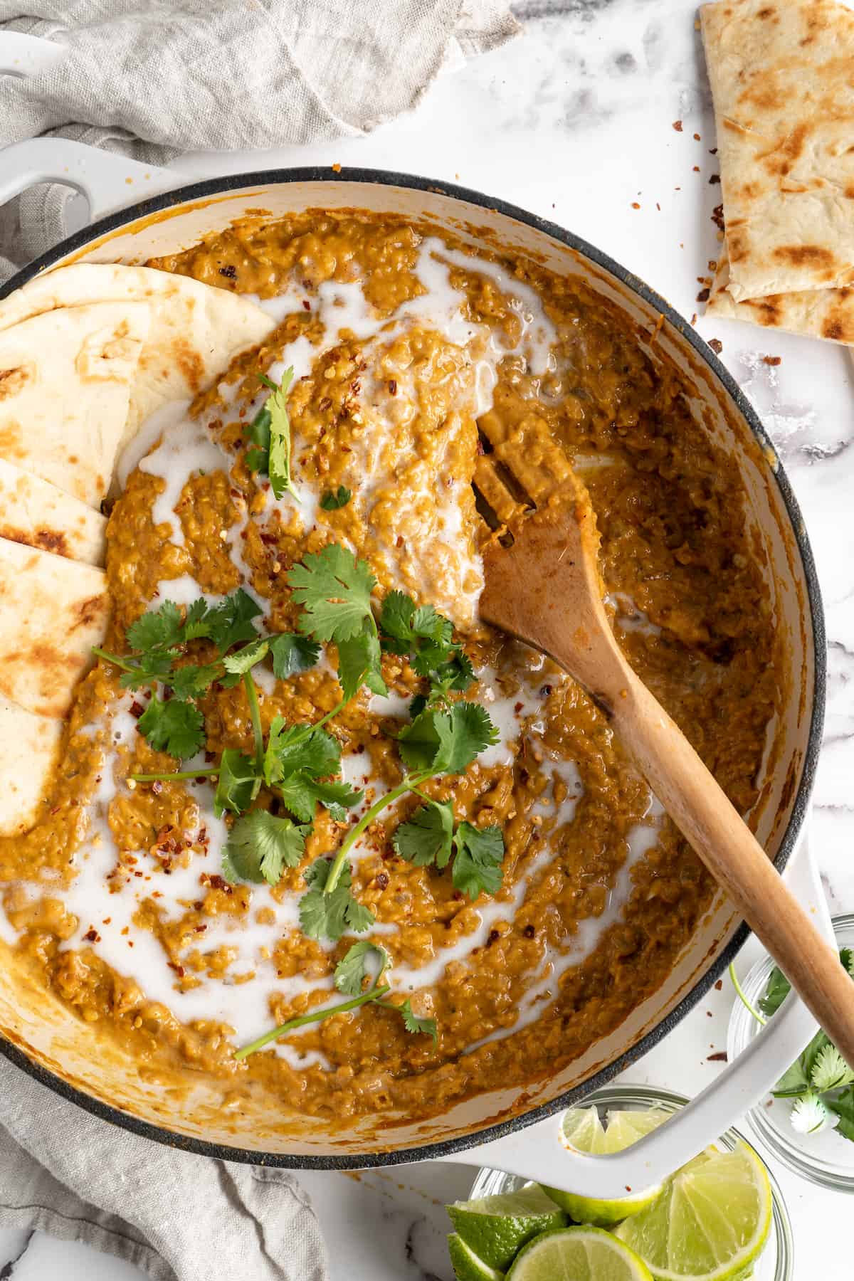 Overhead view of red lentil curry in pot with wooden spoon and naan