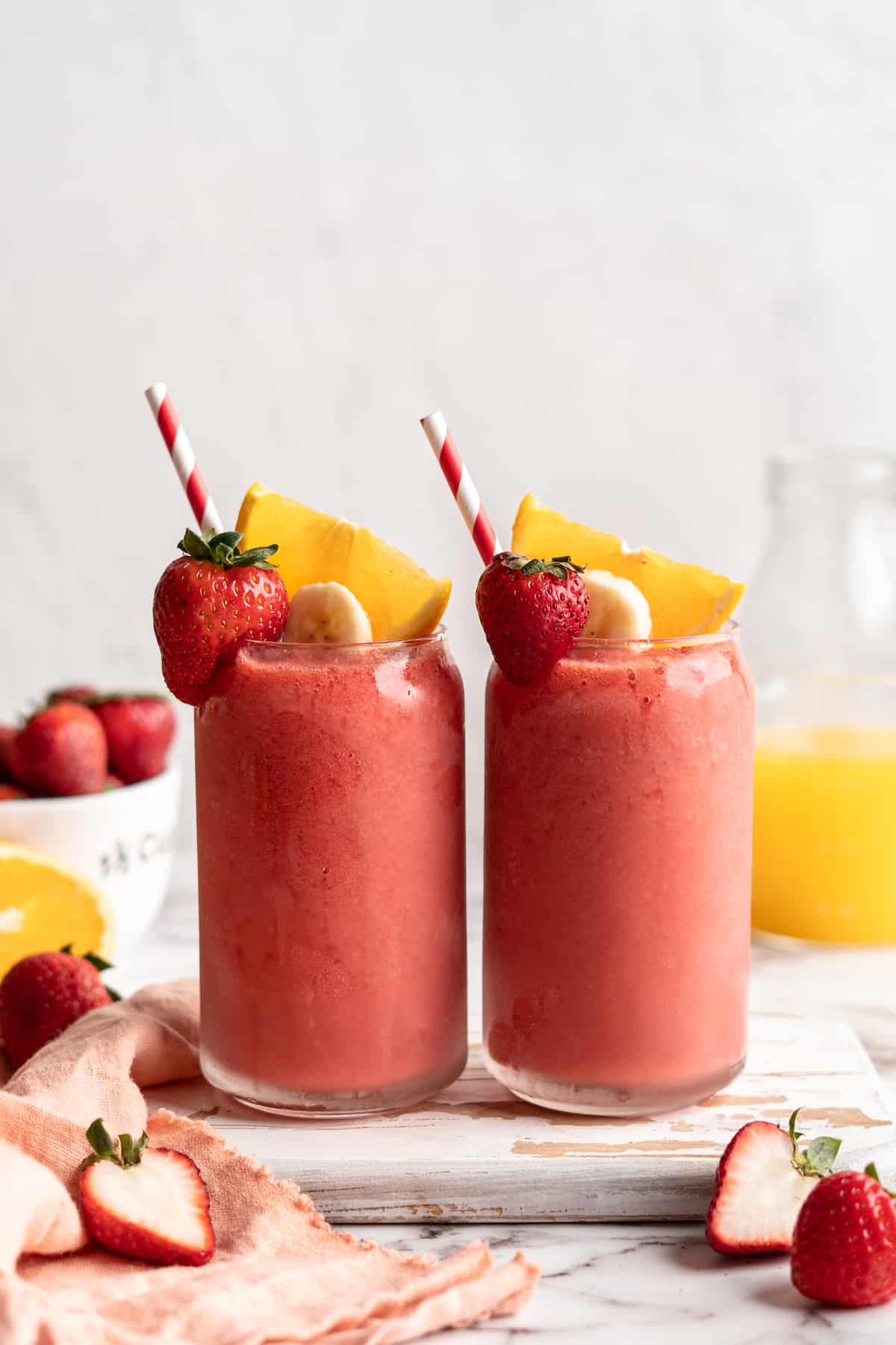 2 glasses of strawberry banana smoothie with straws and fresh fruit for garnish