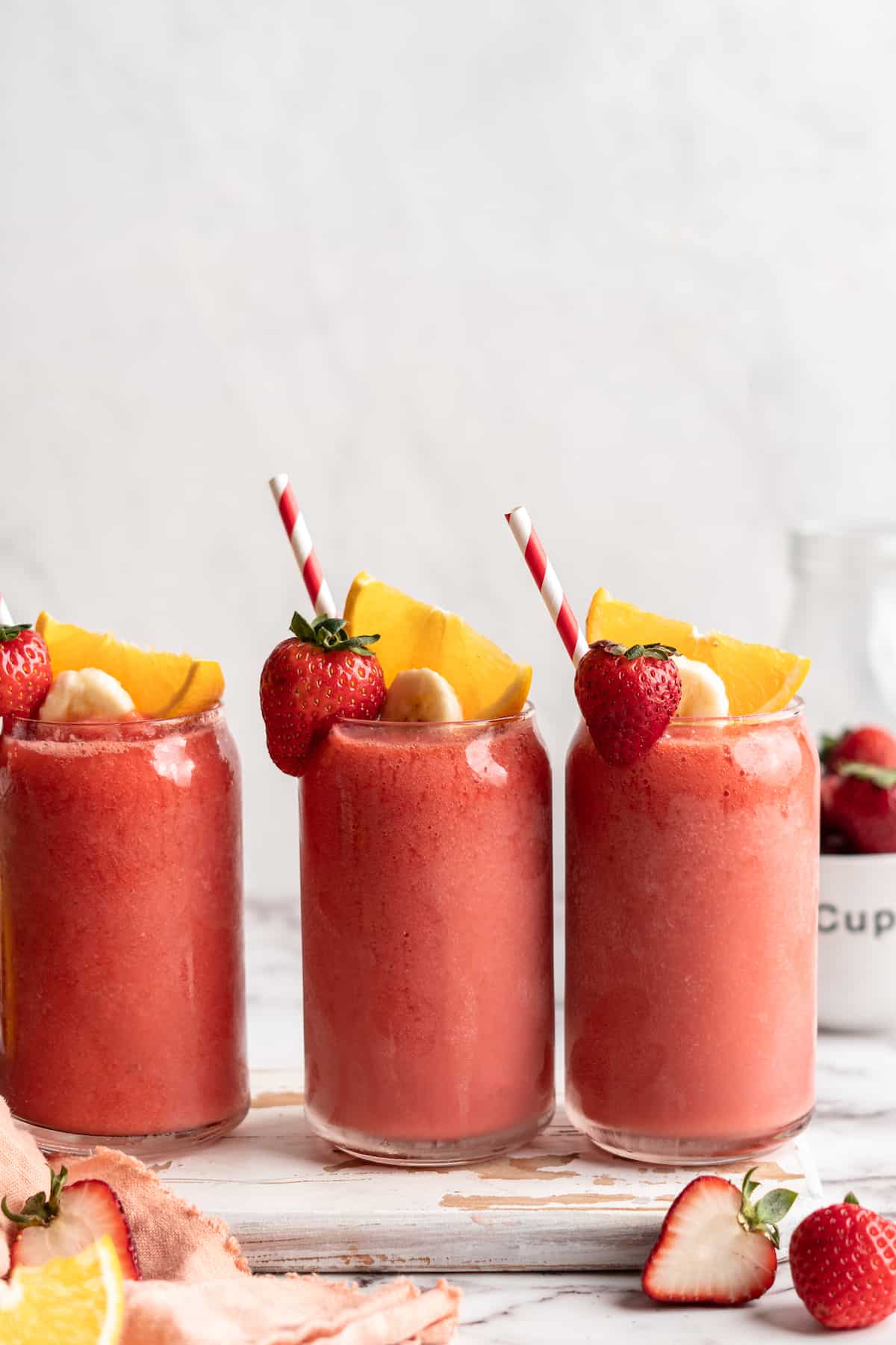 3 glasses of strawberry banana smoothie with straws and fresh fruit garnish