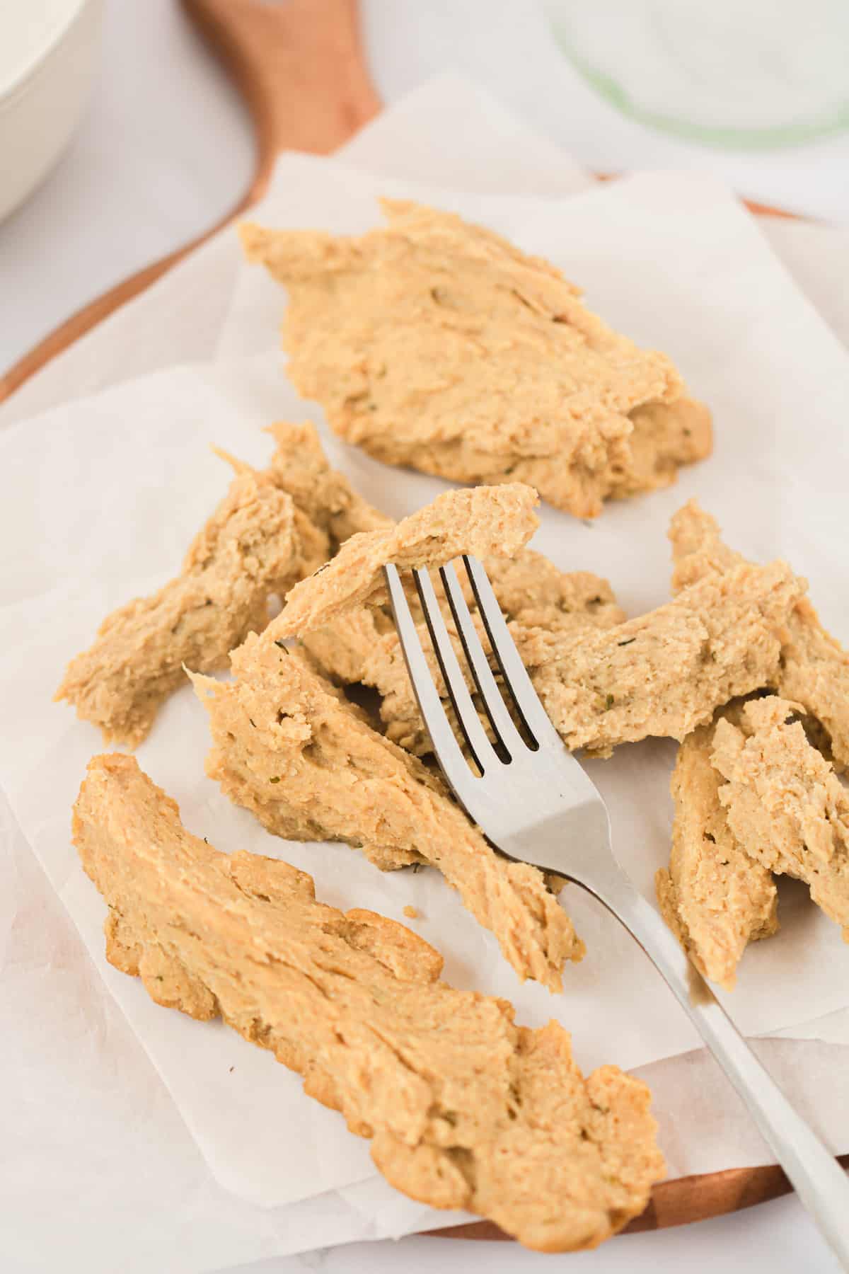 Torn pieces of vegan chicken on parchment paper with fork