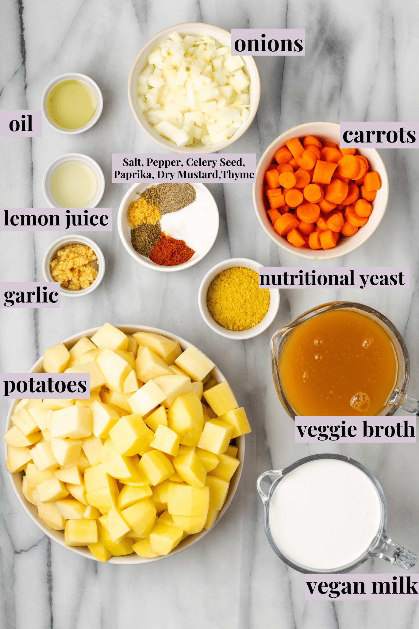 Overhead view of the labeled ingredients needed for potato soup: a bowl of oil, a bowl of onions, a bowl of carrots, a bowl of potatoes, a bowl of veggie broth, a bowl of nutritional yeast, a bowl of vegan milk, a bowl of garlic, a bowl of lemon juice, and a bowl of salt, pepper, thyme paprika, celery seed, and dry mustard
