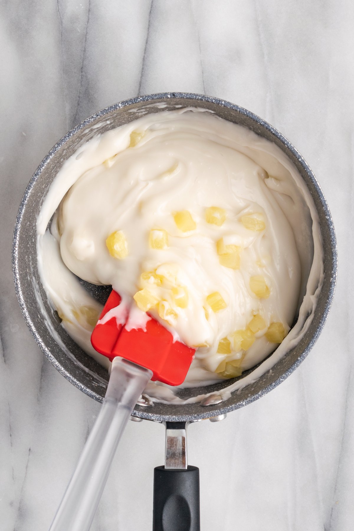 Stirring pineapple into haupia with rubber spatula
