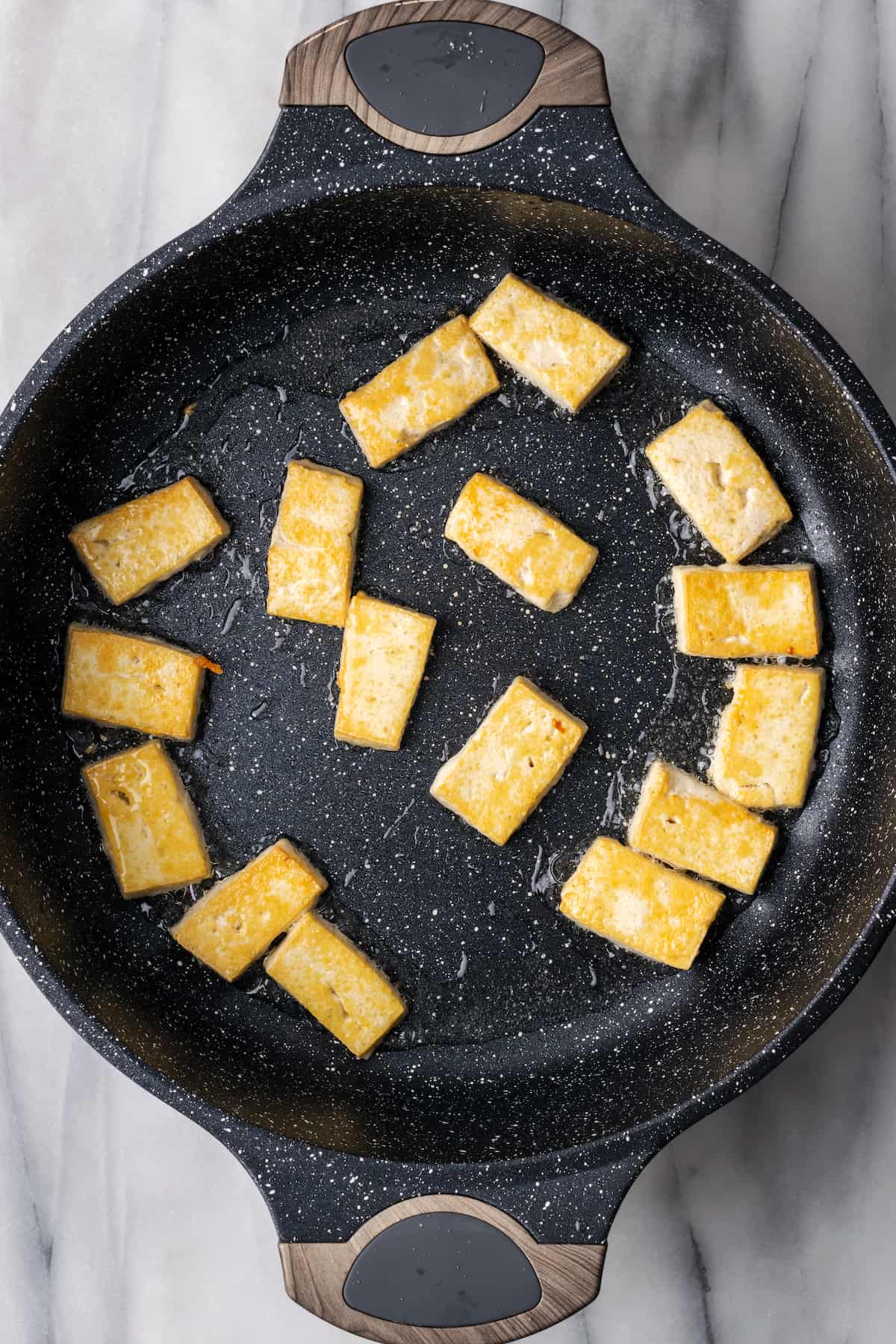 Overhead view of tofu pieces cooking in pan