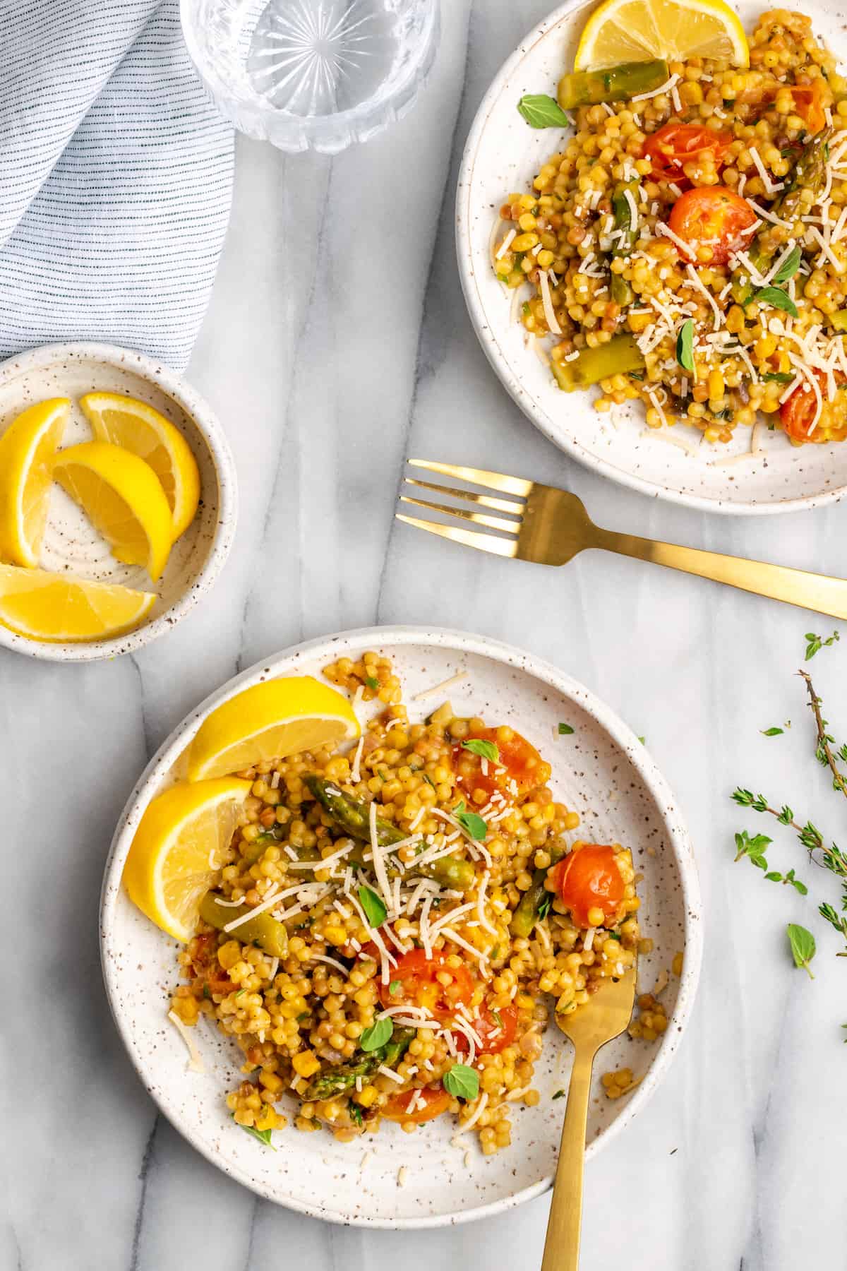 Two plates of Herb & Veggie Fregola with bowl of lemon wedges