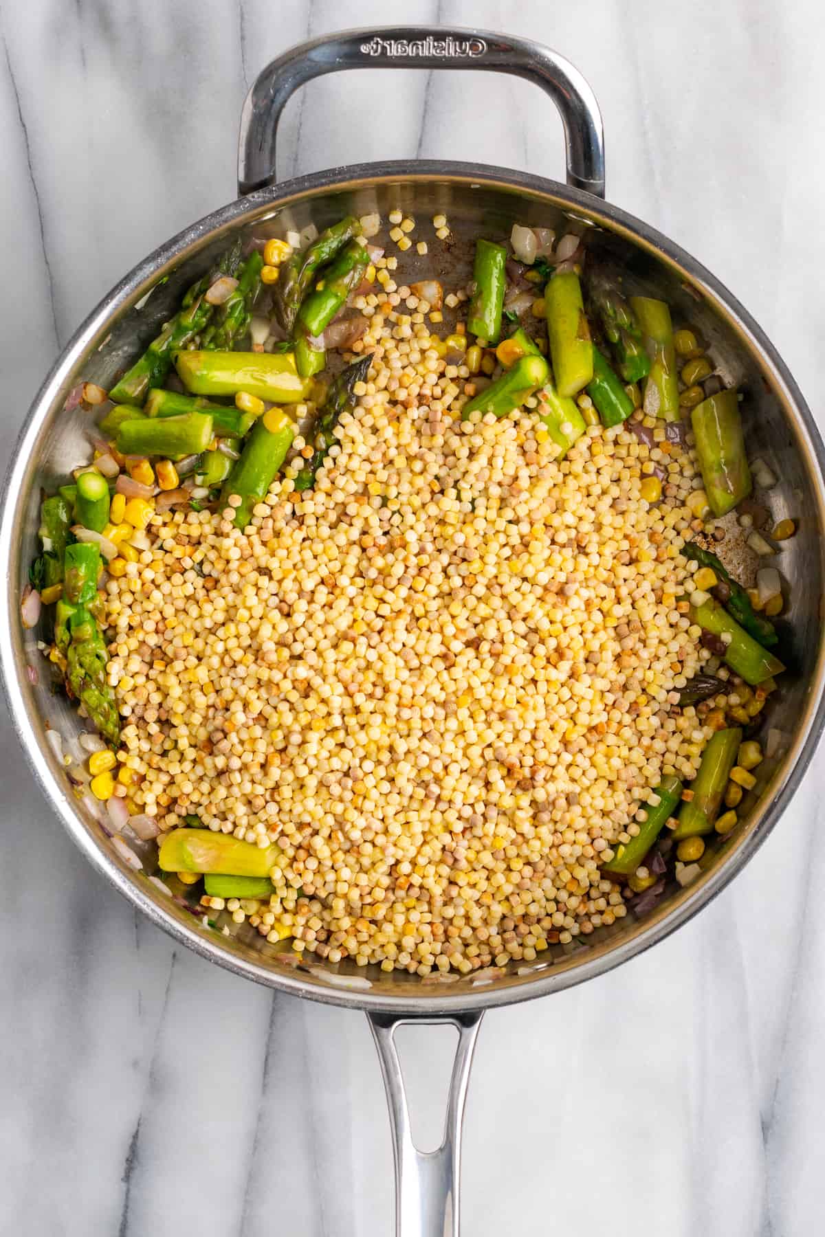 Overhead view of fregola added to skillet of vegetables