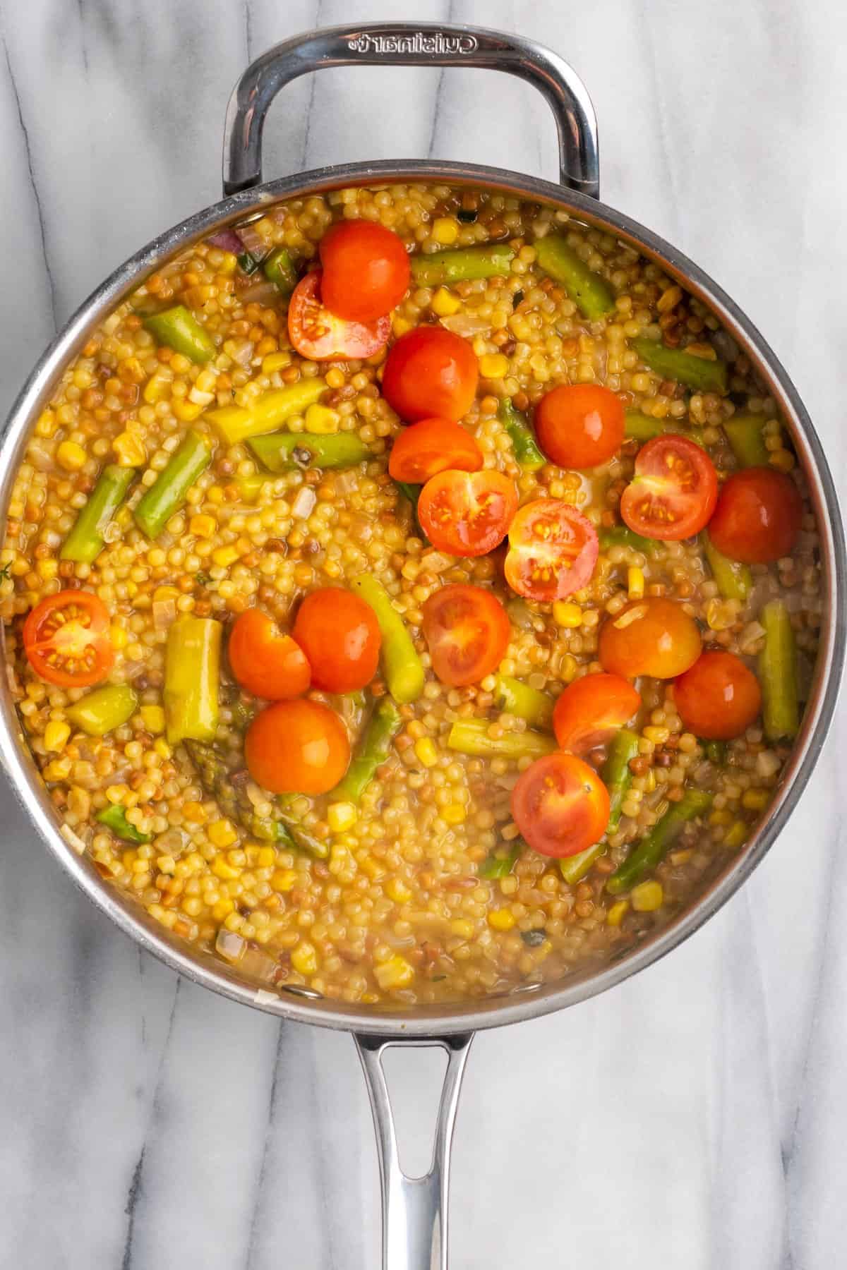 Overhead view of tomatoes added to fregola in skillet