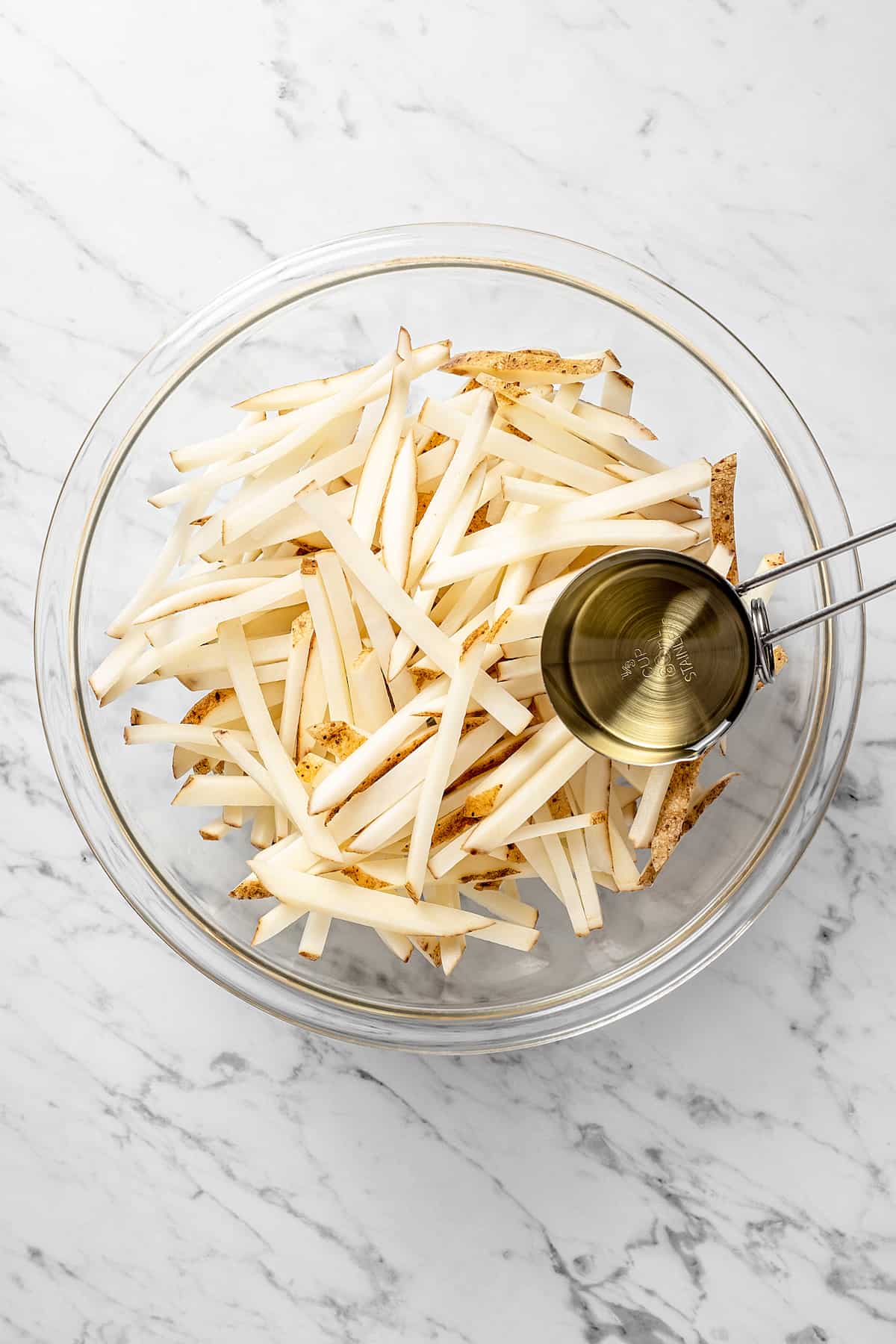 Overhead view of uncooked fries in mixing bowl with oil