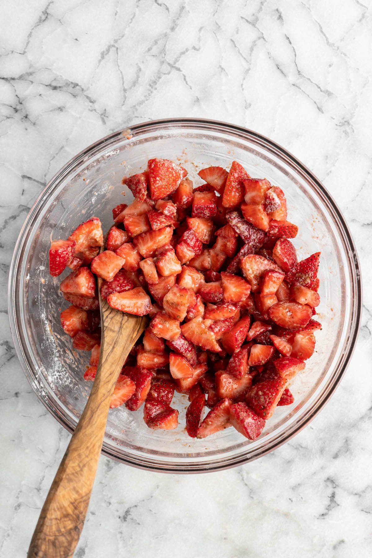 Overhead view of macerated strawberries in glass bowl with wooden spoon