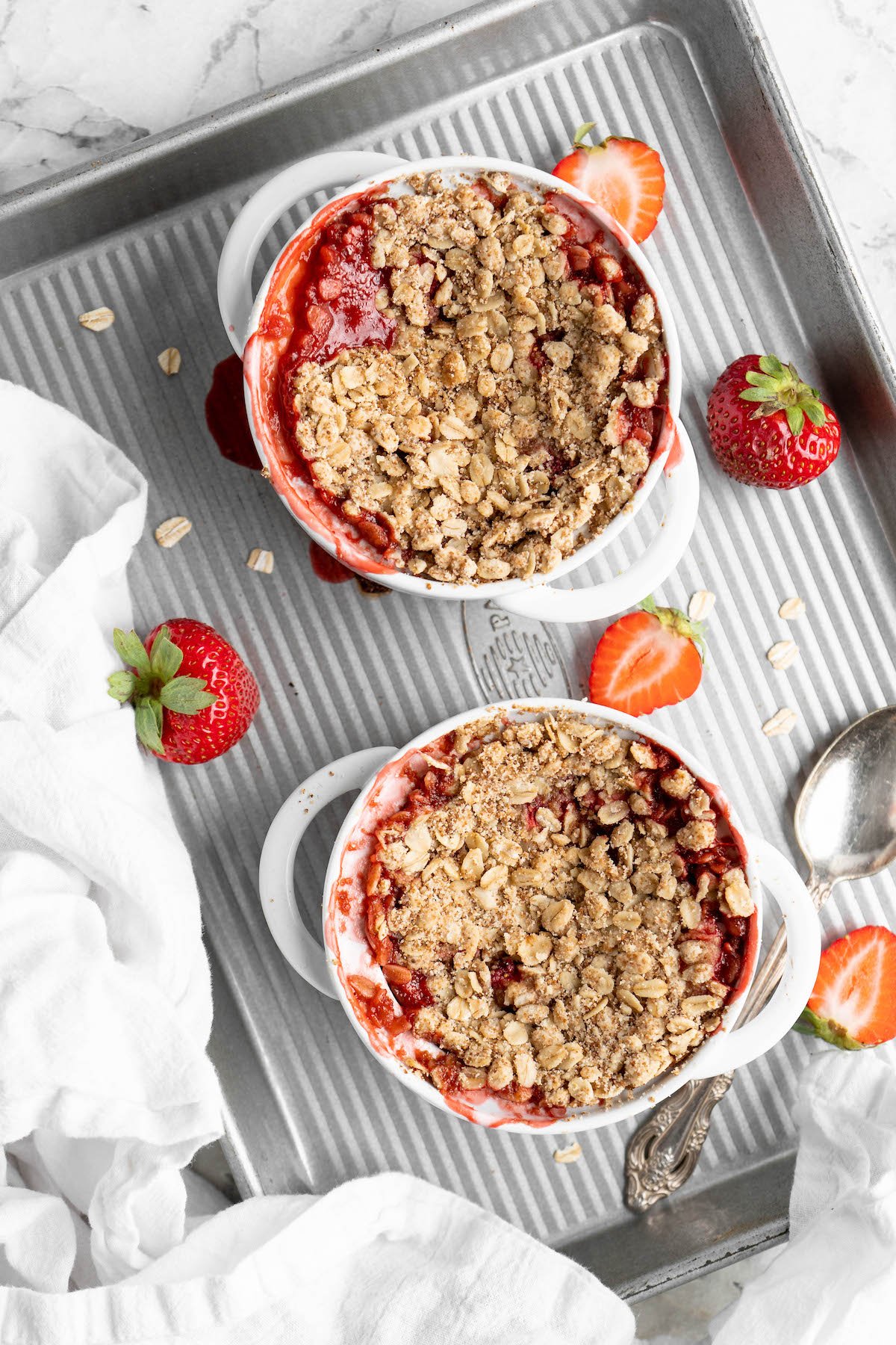 Overhead view of two strawberry crumbles in ramekins on half sheet pan