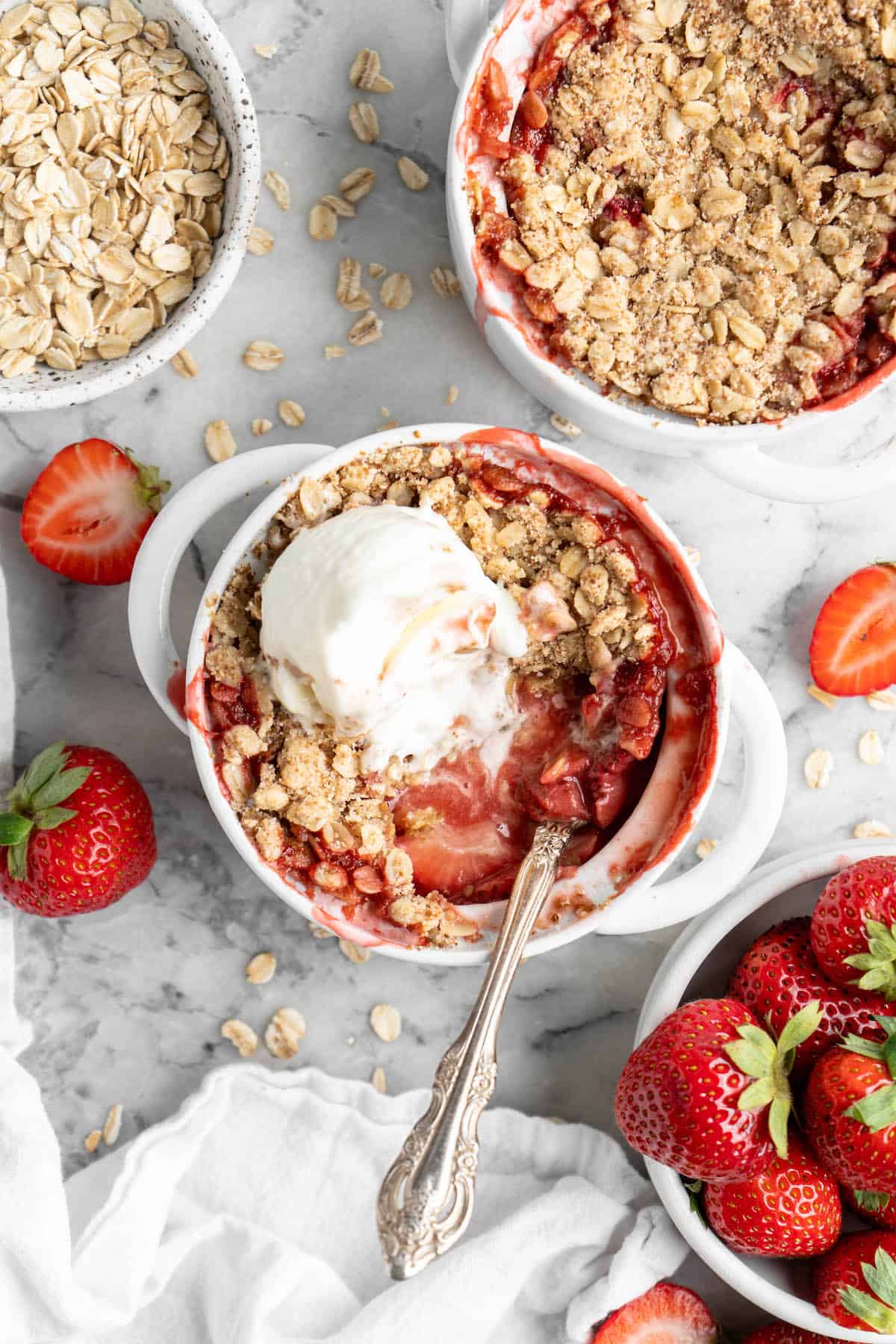Overhead view of strawberry crumble in ramekins, with one topped with vanilla ice cream
