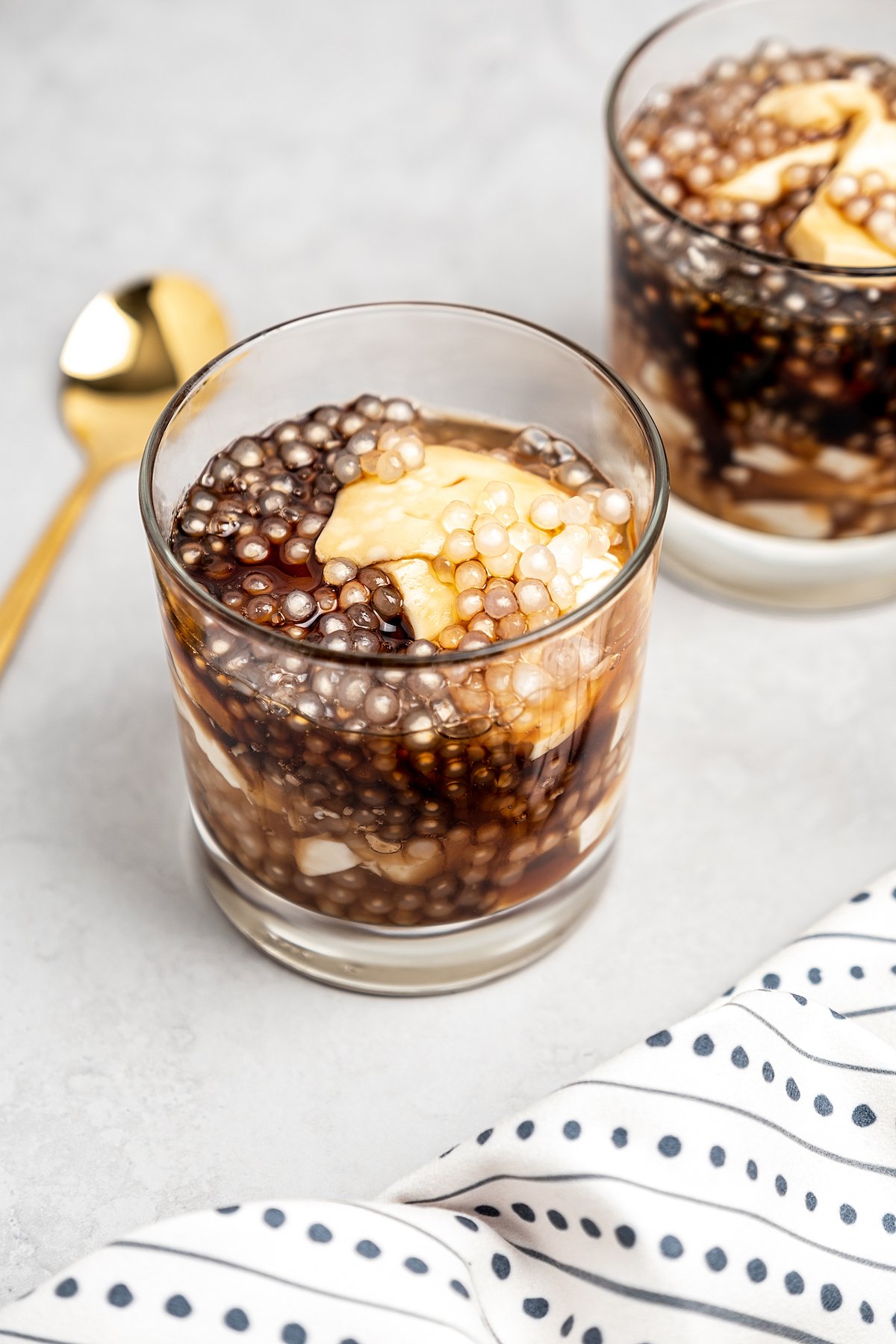Two servings of taho in glasses with napkin and gold spoon