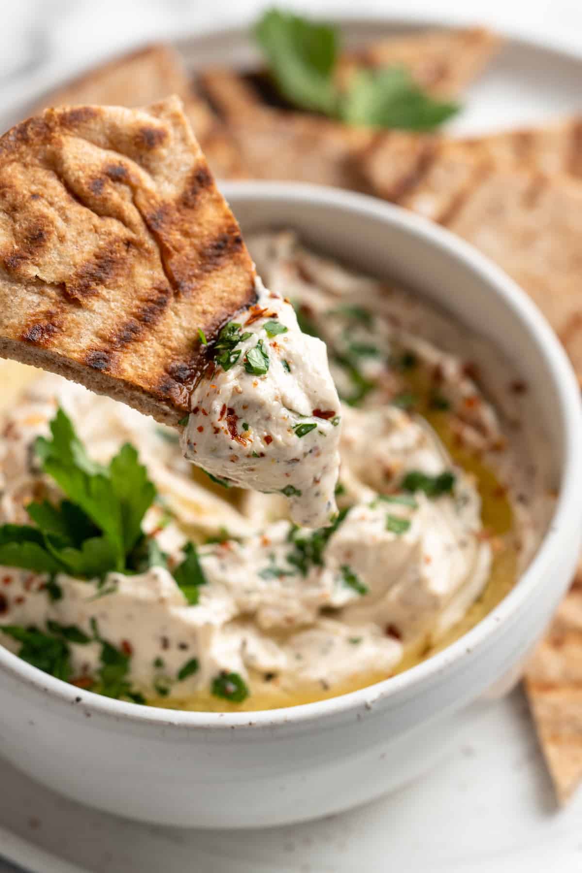 Pita chip with vegan whipped feta dip held over bowl