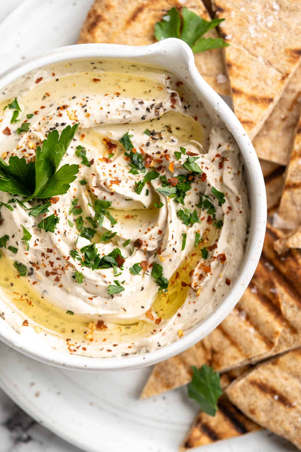 Overhead view of vegan whipped feta dip in bowl on platter of grilled pita chips