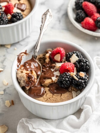 Ramekin of vegan baked oats topped with melted chocolate, berries, and almonds