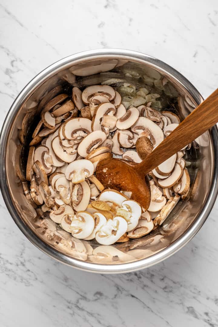 Overhead view of wooden spoon stirring mushrooms in Instant Pot insert