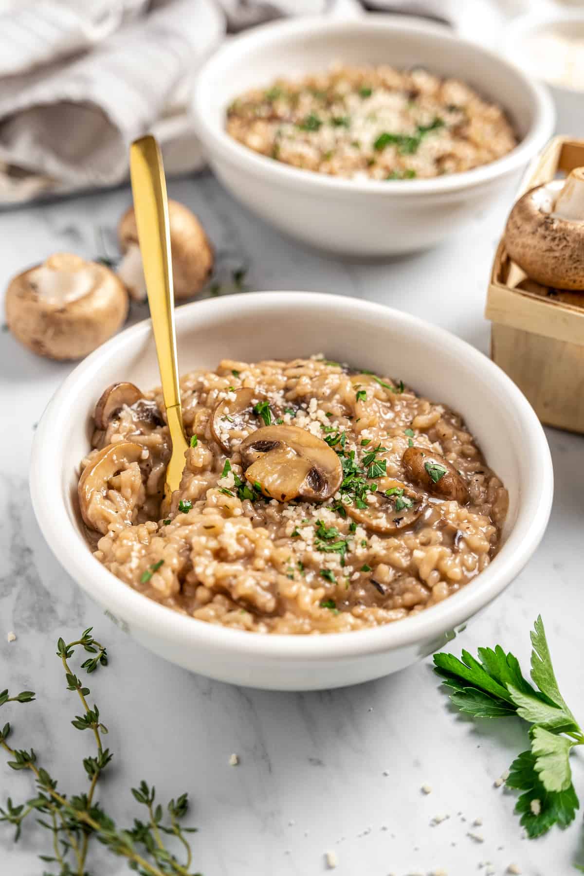 Two bowls of vegan Instant Pot risotto with mushrooms, with fresh herbs and mushrooms on tabletop