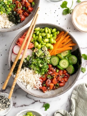 Overhead view of vegan poke bowl with chopsticks on top, surrounded by toppings and garnishes