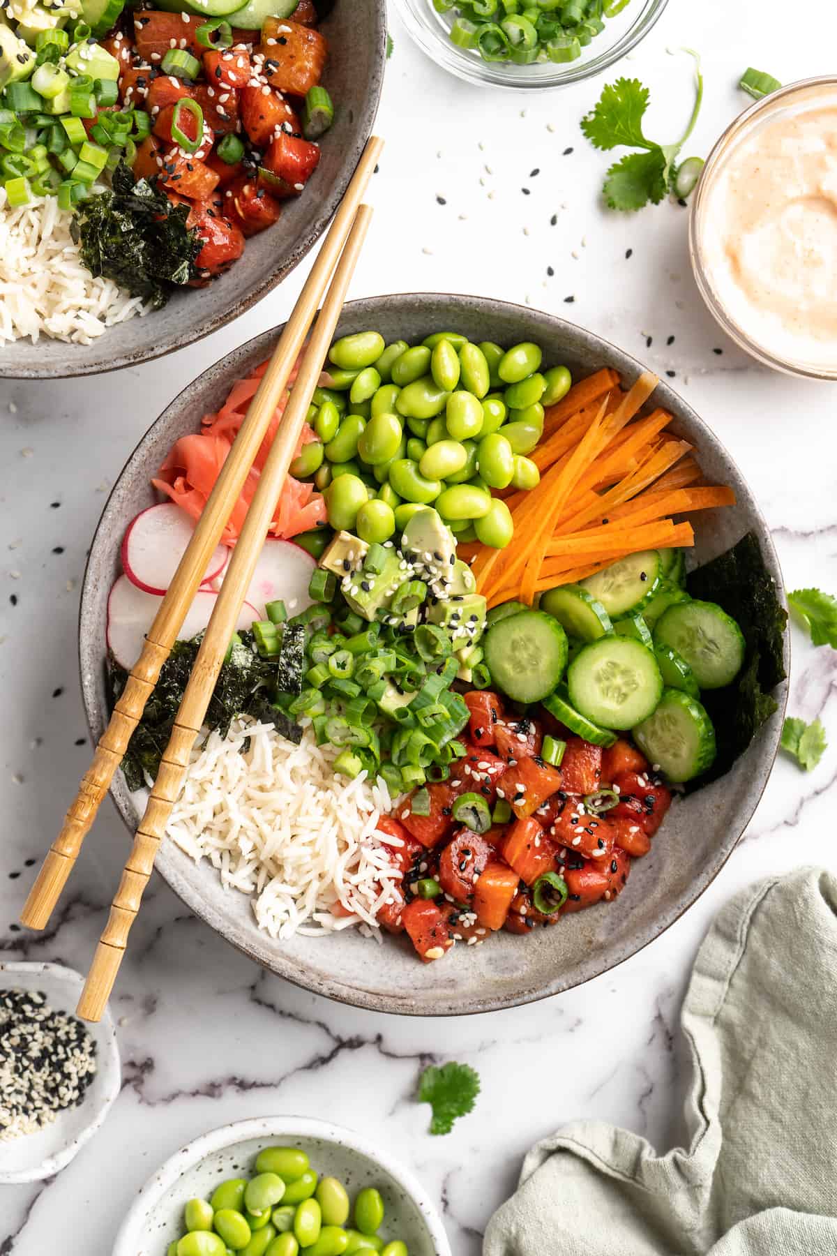 Overhead view of vegan poke bowl with chopsticks on top, surrounded by toppings and garnishes