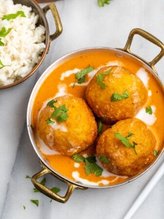 Overhead view of malai kofta in gold serving bowl with cooked rice in second bowl