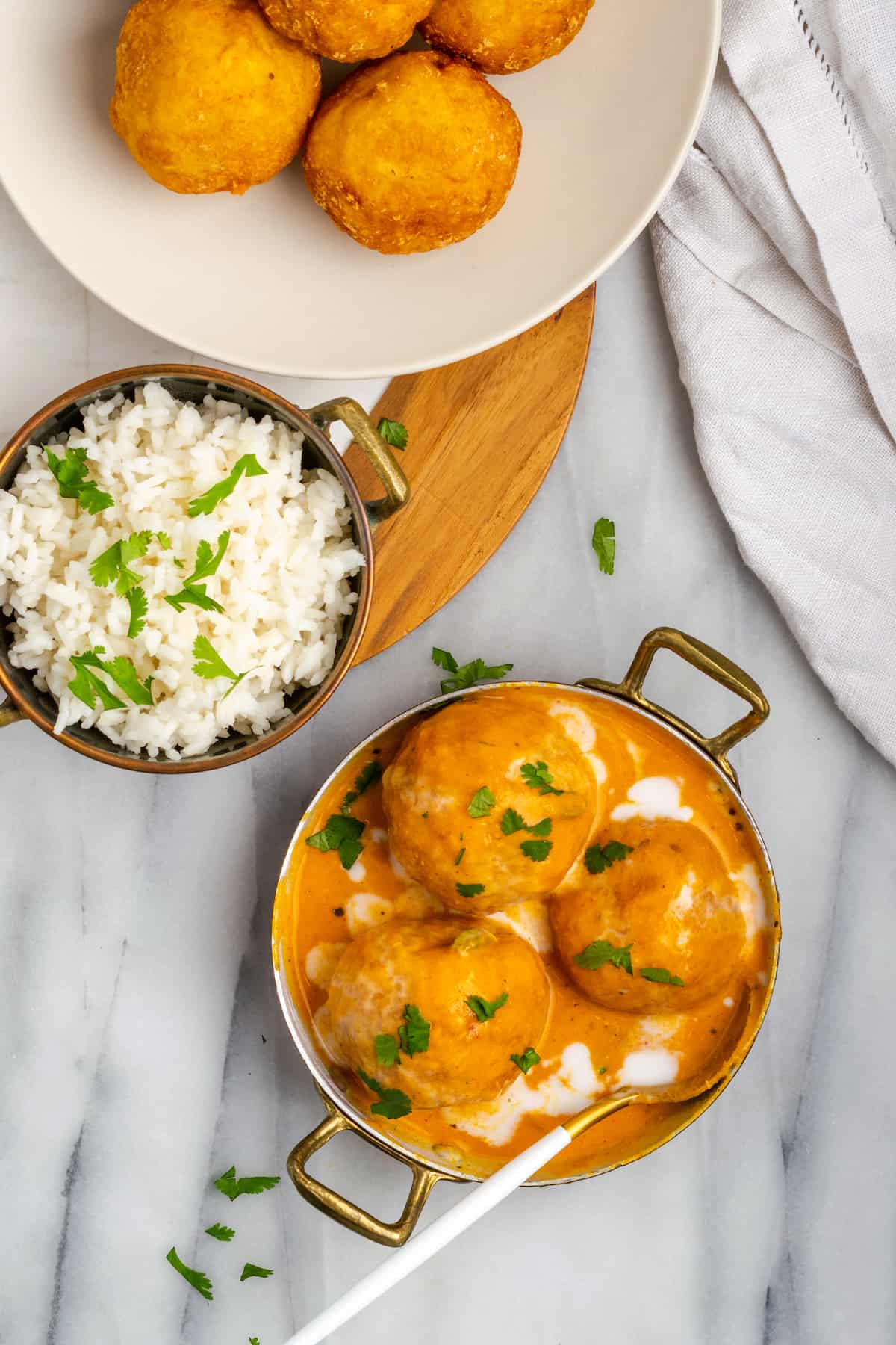 Overhead view of malai kofta in bowl with sauce, with bowl of rice and dumplings