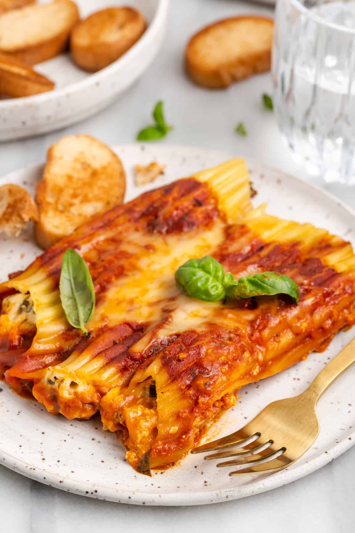 Plate of vegan manicotti with garlic bread and basil garnish