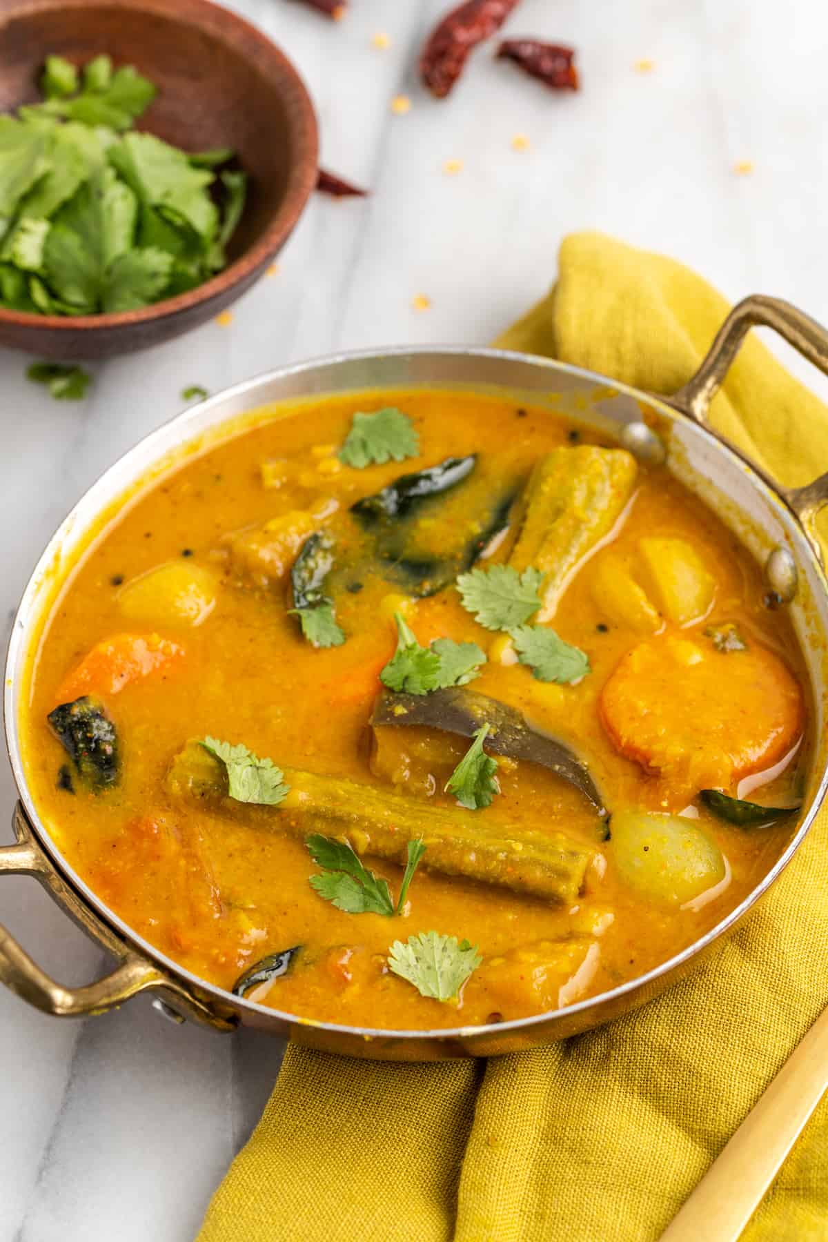 Vegan sambar in gold serving dish, with cilantro leaves scattered on top for garnish