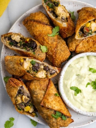 Overhead view of vegan southwest egg rolls on serving plate, with some cut open to show filling