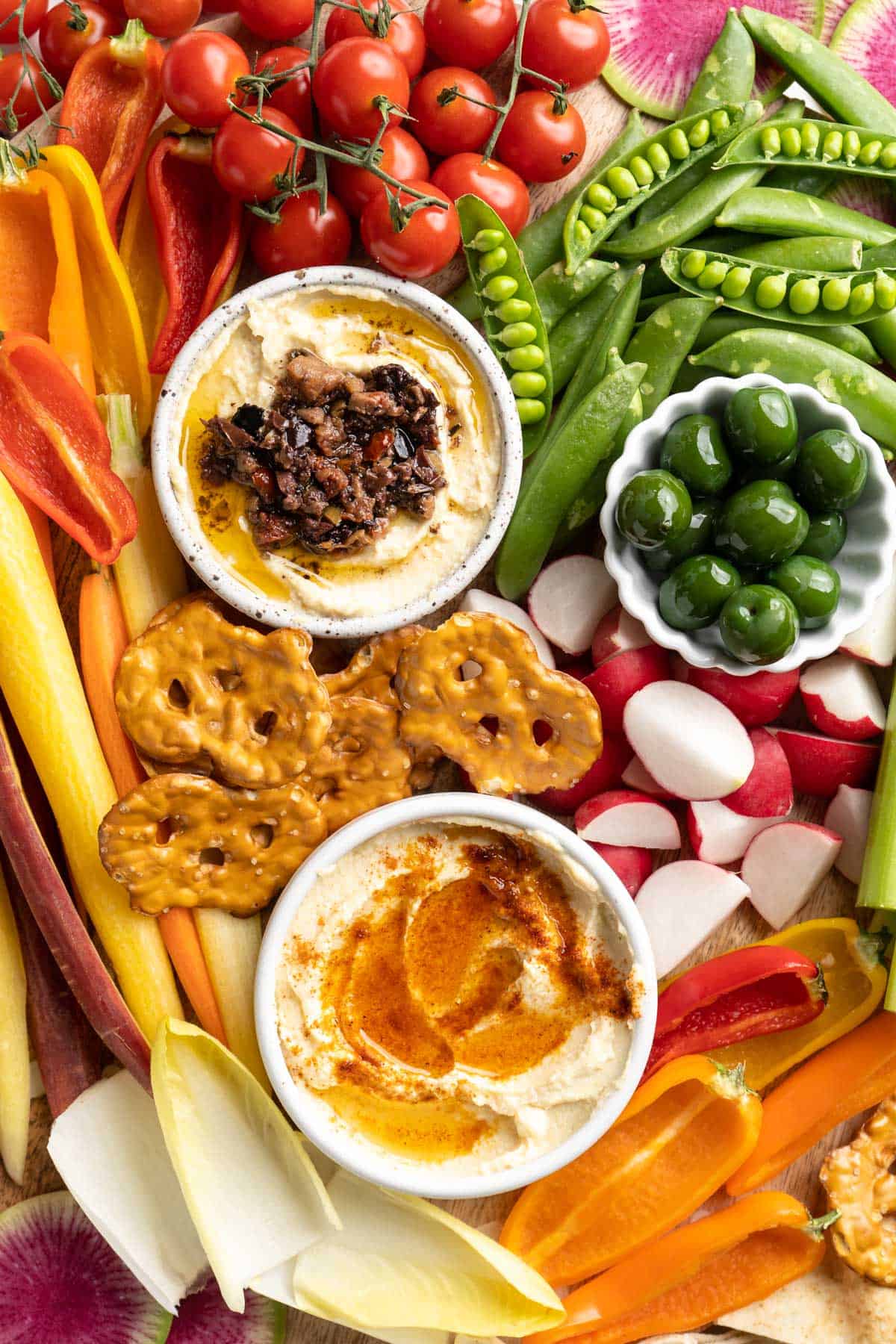 Overhead view of crudité platter with bowls of hummus and green olives