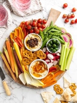 Overhead view of vegetable crudité platter with bowls of hummus and olives