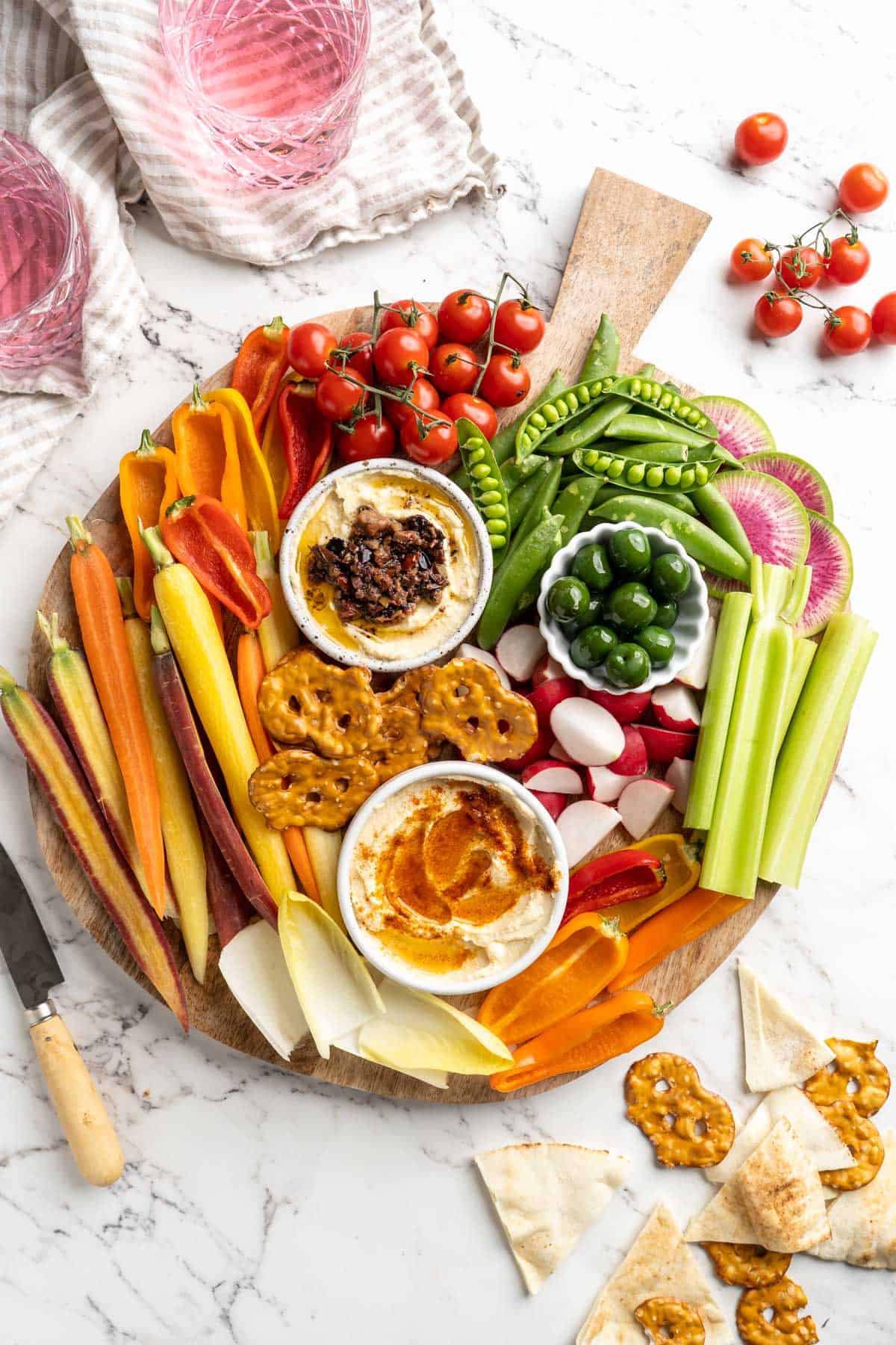 Overhead view of vegetable crudité platter with bowls of hummus and olives