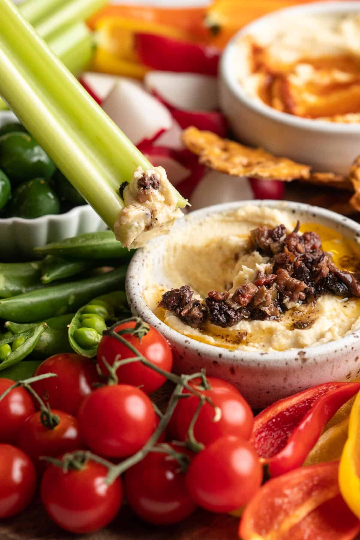 Dipping celery into hummus topped with olive tapenade