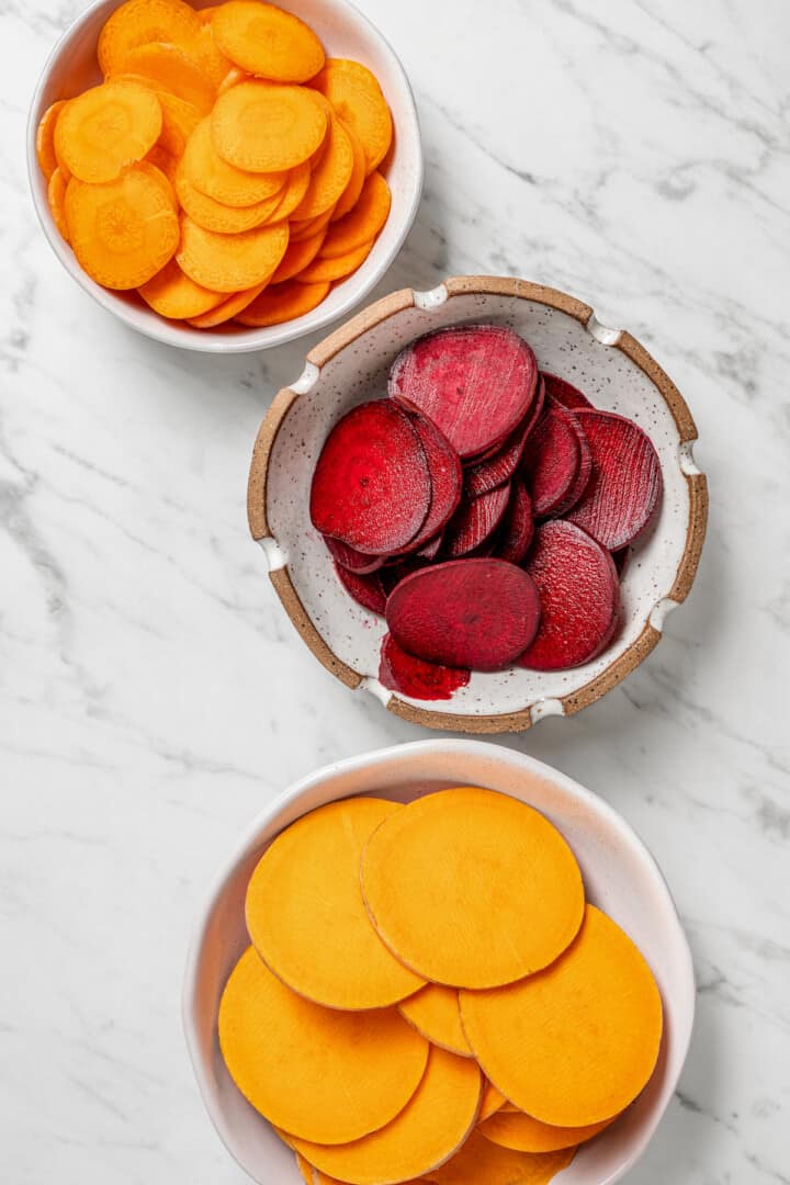 Overhead view of sliced beets, carrots, and sweet potatoes in bowls