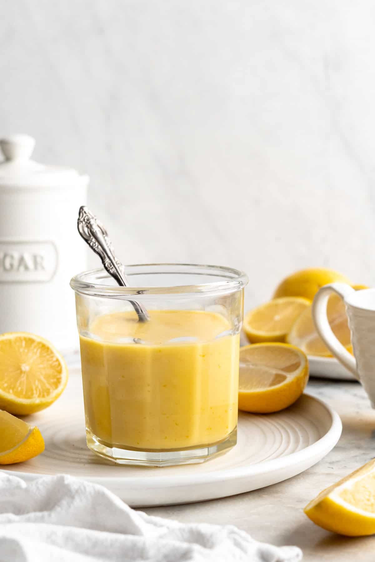 Jar of vegan lemon curd with spoon on plate with halved lemons