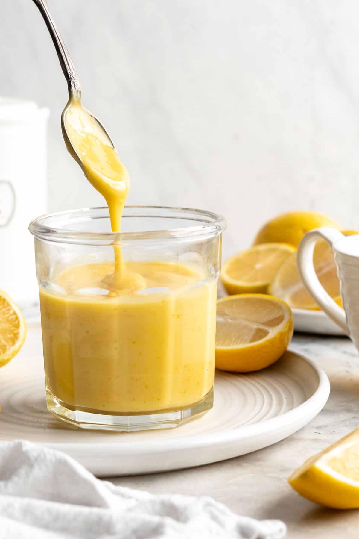Spoon drizzling vegan lemon curd back into jar set on plate