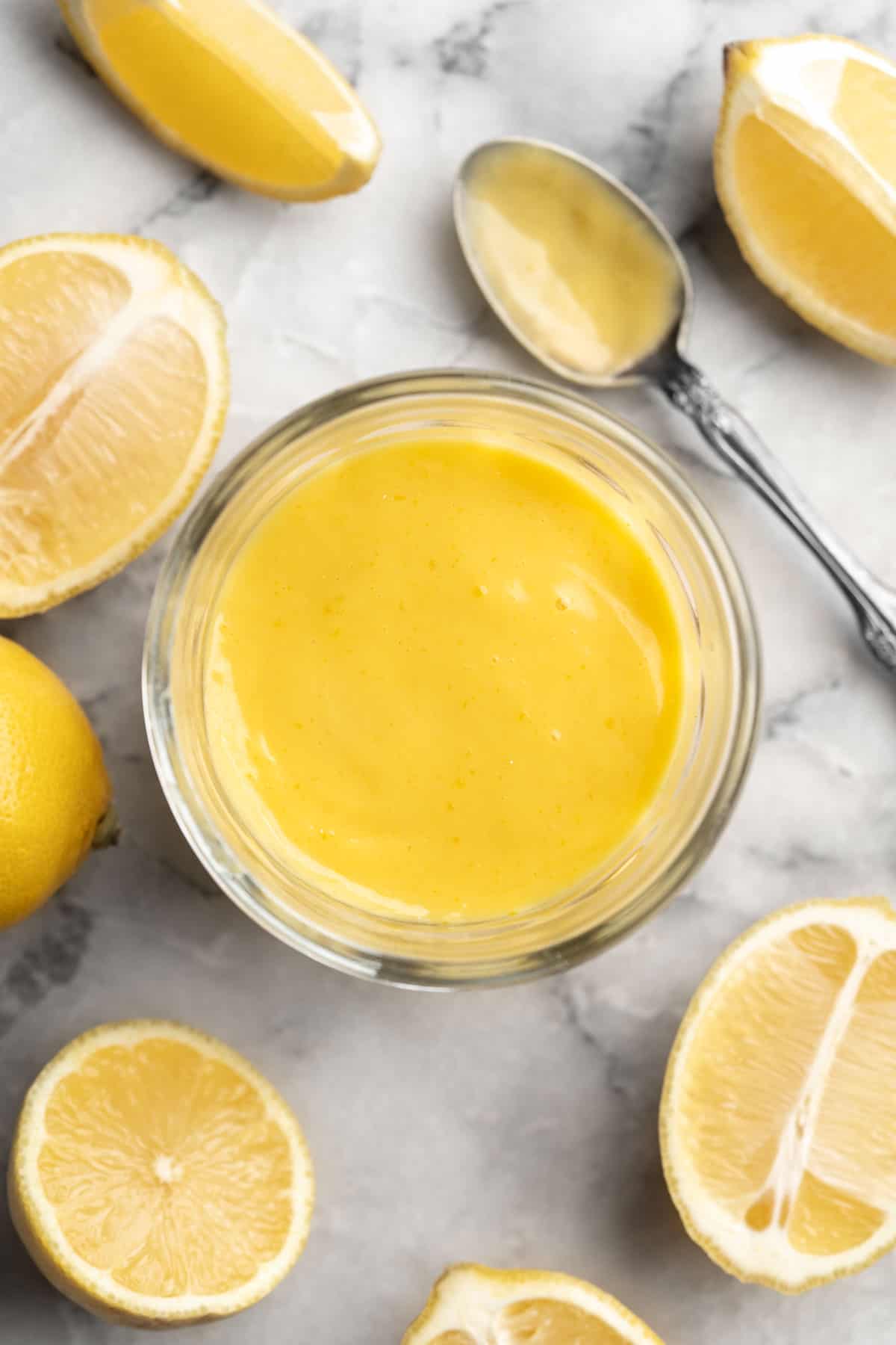 Overhead view of vegan lemon curd in jar, surrounded by halved lemons