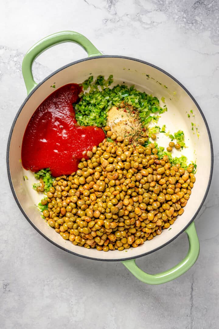 Overhead view of tomato sauce, peas, spices, and sofrito in enamel Dutch oven