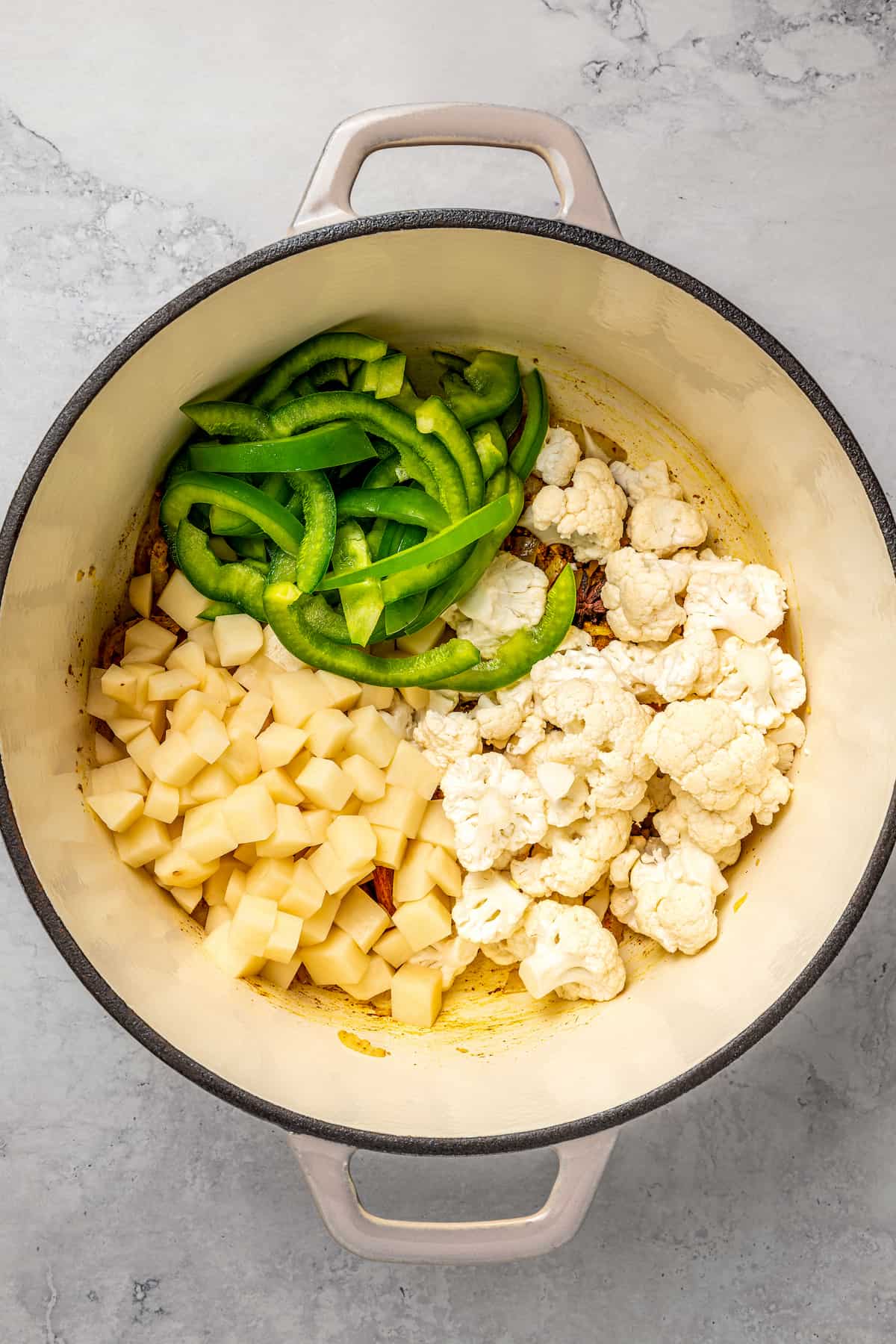 Diced potatoes, cauliflower florets, and green bell pepper strips in pot