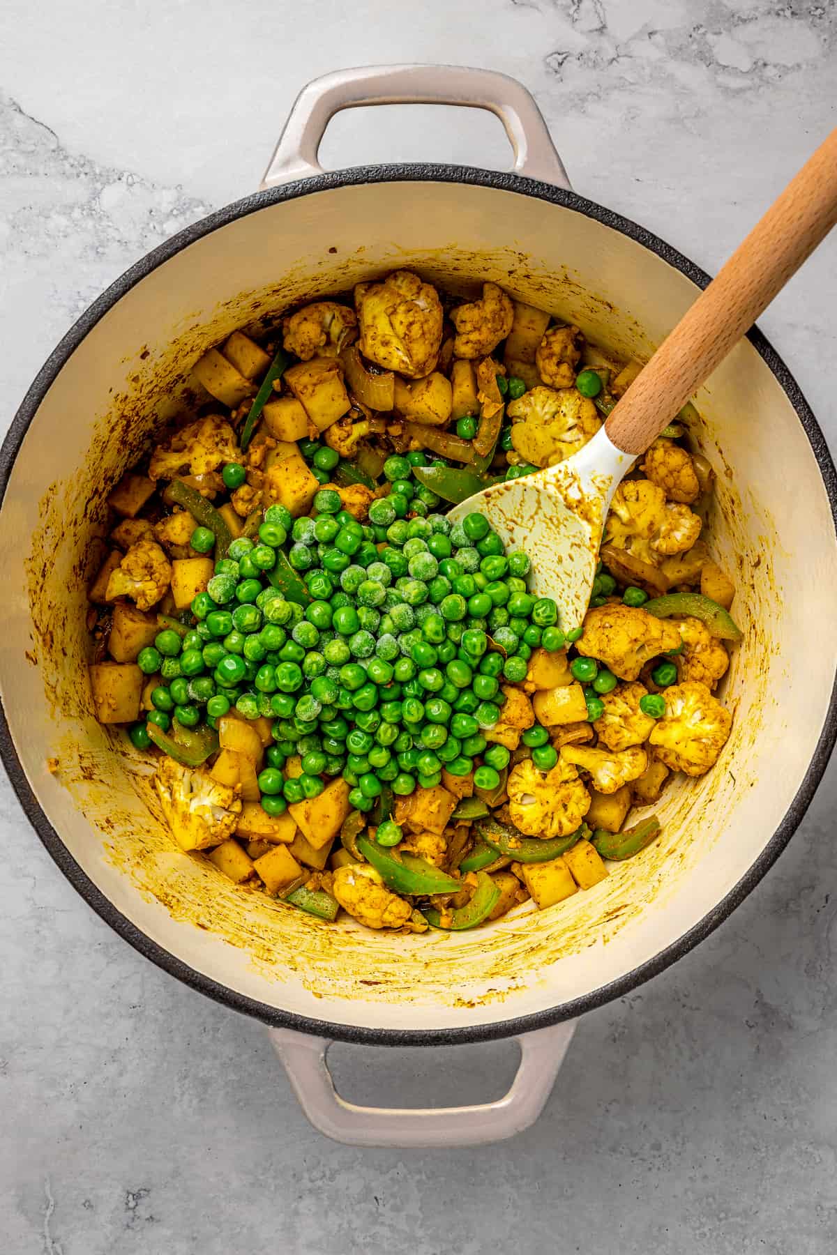 Stirring peas into pot of cooked vegetables