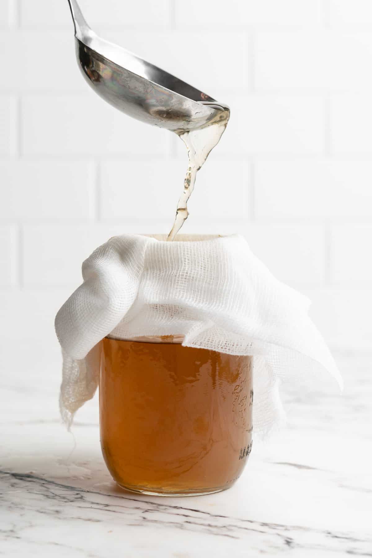 Ladling vegetable broth into jar topped with cheesecloth