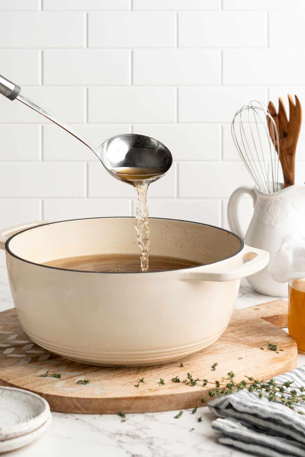 Ladle pouring vegetable broth into white enamel pot