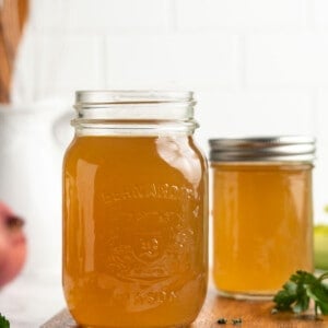 Two jars of homemade vegetable broth on wood cutting board