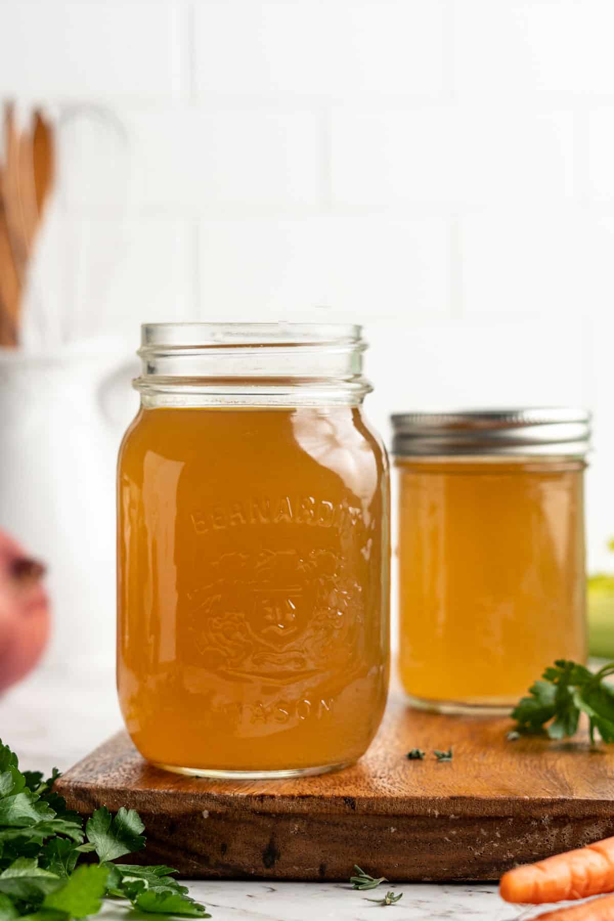 Two jars of homemade vegetable broth on wood cutting board