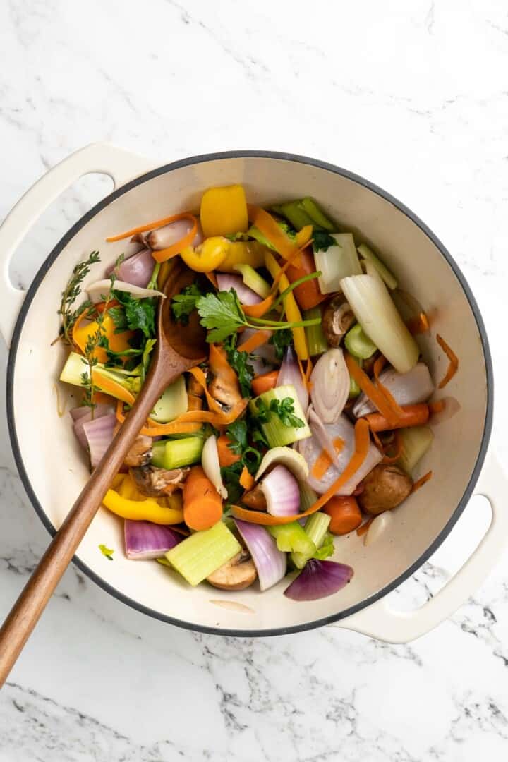 Overhead view of ingredients for vegetable broth in pot with wooden spoon